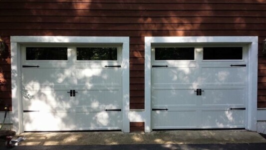 Garage with two white wooden garage doors with black accents and windows.